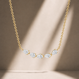 A delicate yellow gold chain necklace featuring five small, bezel-set round clear gemstones in a curved row, displayed against a warm beige background with soft diagonal shadows.